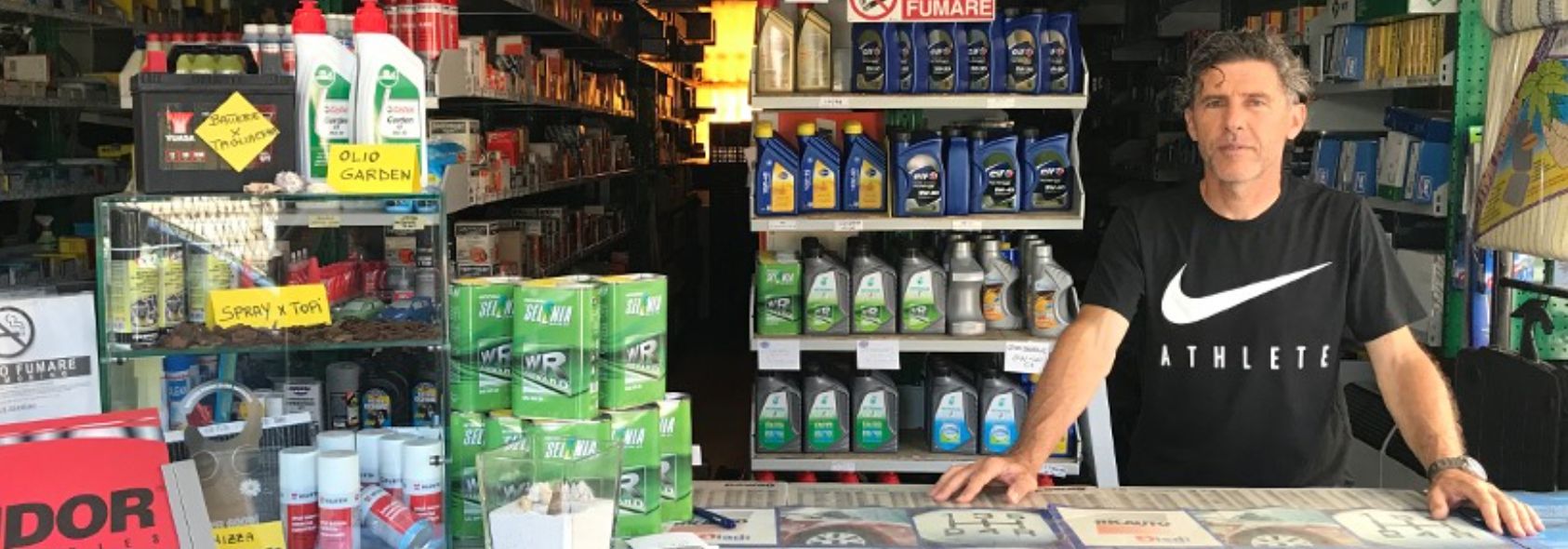 Alessandro Milan al bancone del negozio, con gli scaffali di olio motore e ricambi alle spalle